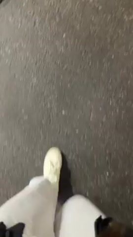 The video starts with a first-person view of someone walking on a paved surface at night. The camera then pans to show a white car being towed on a flatbed trailer. The trailer is moving on a road next to a sidewalk. The camera follows the trailer as it drives by, and then pans to show a brightly lit convenience store with a Christmas tree in front. The store has a green sign that reads "Green". The scene is dark, suggesting nighttime.