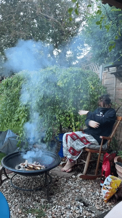 Woman tends smoky backyard fire pit in Stotfold