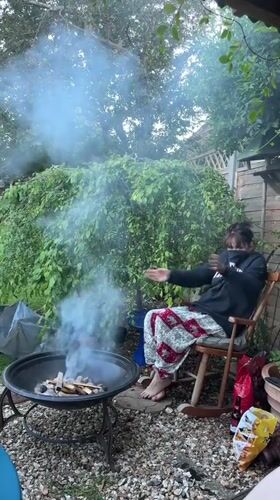 Woman tends smoky backyard fire pit in Stotfold