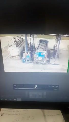 A video shows a monitor displaying what appears to be security camera footage from a gas station. A truck is parked between two gas pumps. Suddenly, there is an explosion with flames and smoke engulfing the area. The explosion obscures the view for several seconds. Papers with handwritten text can be seen in front of the monitor.