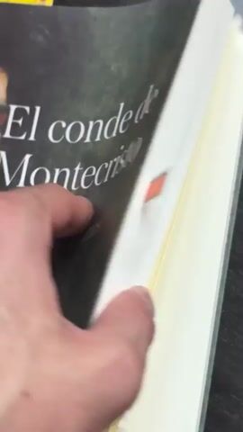 The video shows a close-up of someone flipping through the pages of a book written in Spanish. The book has a green cover.  The pages are thin and white with black text. The background is a dark surface.  The person's fingers are visible on the left side of the frame as they quickly turn the pages.