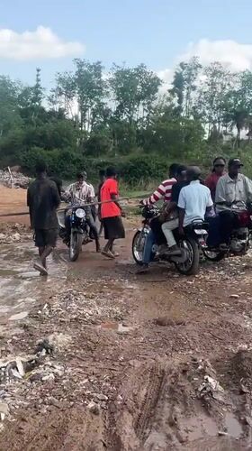 People gather with motorbikes on muddy road in Abuja