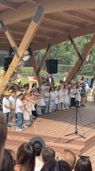 Children perform on stage in Serbia wearing white, hats