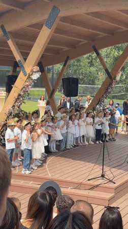 Children perform on stage in Serbia wearing white, hats