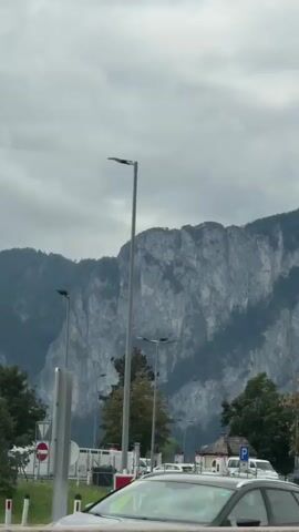 The video shows a cloudy day with a large mountain range in the background. In the foreground, there is a highway with cars and trucks. There are also signs for a rest stop, indicating gas, food, and lodging. The camera pans from left to right, capturing the scenic view and the services available to travelers.