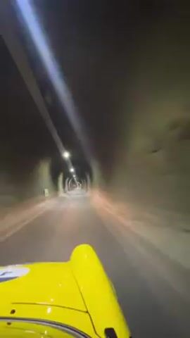 The video shows a car driving through a tunnel. The car is yellow. The tunnel is lit by overhead lights. The camera is mounted on the car, capturing the view from the driver's perspective.