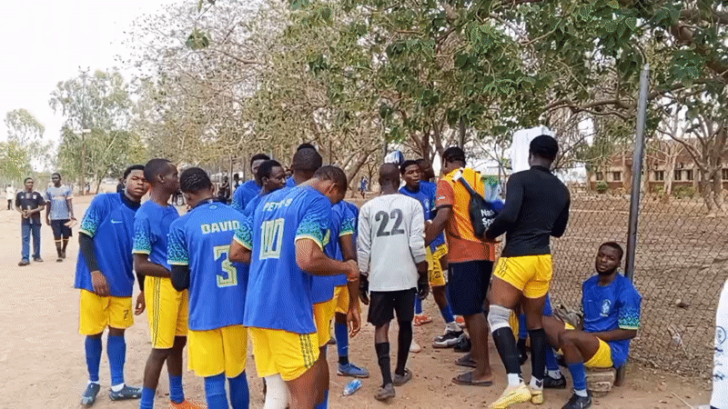 Soccer players gather after game on dirt field in Minna