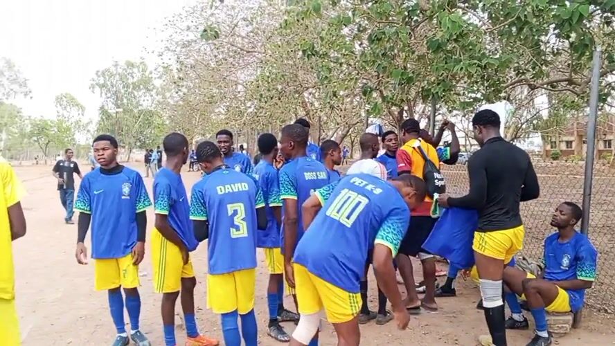 Soccer players gather after game on dirt field in Minna