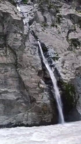 Waterfall crashes down rocky cliff into turbulent river, Shansha