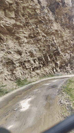 Wet dirt road winds past eroded rock face near Tandi