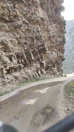 Wet dirt road winds past eroded rock face near Tandi