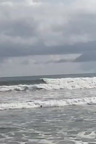 The video shows a choppy ocean with waves rolling in towards the shore. The sky is overcast with dark, heavy clouds, suggesting an impending storm or a gloomy day. The waves are not particularly large but are clearly visible, with white foam cresting as they break. The water appears greyish-blue, reflecting the dull sky. The overall scene depicts a somewhat rough sea under a cloudy atmosphere. There are no people or objects visible in the frame, only the natural elements of the ocean and sky.