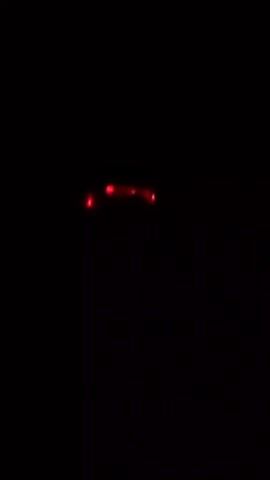 The video depicts a dark scene with several small, blurry lights. The lights flicker and change color, transitioning between green, red, and blue. The lights appear to be clustered together but without clear shape or pattern.