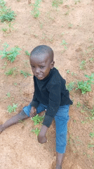 Kids on a dirt path in Baltap, one hauling a backpack sprayer