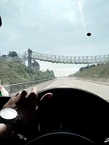 Driver travels highway near suspension bridge in Lamtamot, Indonesia