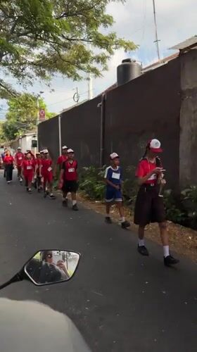 Red-shirted group marches in Kuta while calf grazes nearby