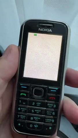 A hand holds a black and silver Nokia feature phone against a light-colored background, possibly a curtain. The phone powers on, displaying the Nokia logo with two hands shaking. The screen then shows the text "Мой господин".