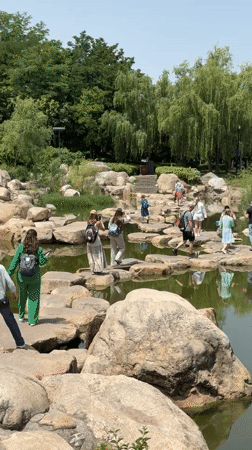 Park visitors cross pond via stepping stones in Yanta District