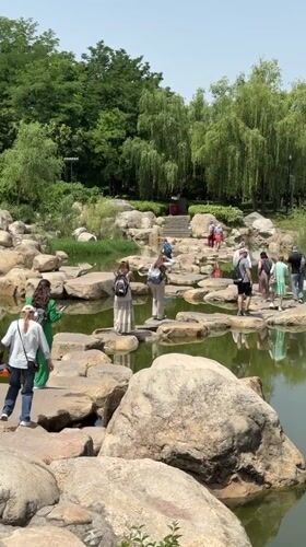 Park visitors cross pond via stepping stones in Yanta District