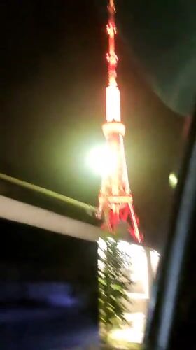 Tall tower glowing red and yellow, seen from a moving vehicle at night