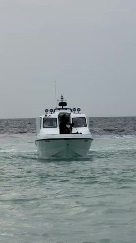 A small white boat bobs in the wavy, grey-green sea under an overcast sky. A person, partially obscured by the boat's structure, leans out and attaches a black fender to the side of the boat.