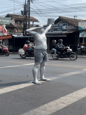 Silver-painted street performer works a pedestrian crossing in Sinduadi