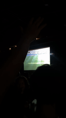 Crowd gathers in dark room to watch soccer on big screen