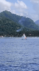 Sailboat spotted off tropical Karangasem coastline near cliffside buildings