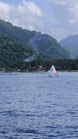 Sailboat spotted off tropical Karangasem coastline near cliffside buildings