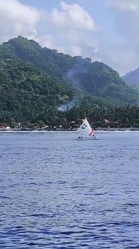 Sailboat spotted off tropical Karangasem coastline near cliffside buildings