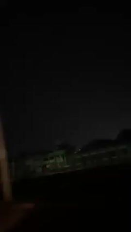 A night-time car ride. Initially, the view is out the passenger window, showing dark buildings with dim lights. The view then switches to the windshield, showing a highway with other cars visible by their headlights and tail lights. The remaining shots are inside the vehicle, facing forward. Details inside the car are mostly obscured by darkness. Music and speech can be heard.