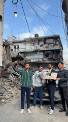 Young men pose with flowers near damaged Gaza building