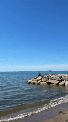 Person sits on rocks by calm waters in Tarquinia