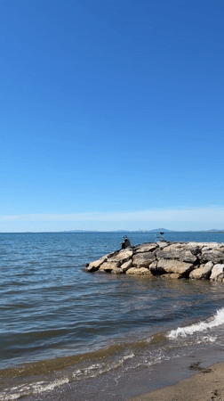 Person sits on rocks by calm waters in Tarquinia