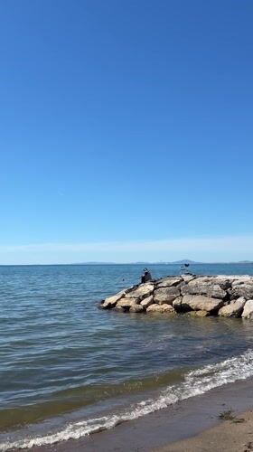 Person sits on rocks by calm waters in Tarquinia