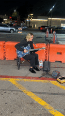 Wheelchair musician performs on LA street near neon-lit storefronts