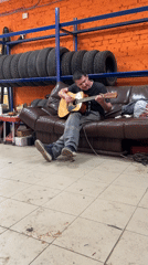 Man plays acoustic guitar on couch in Chaikovsky, Russia