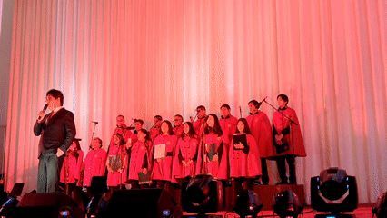 Red-robed choir performs with suited speaker in Cusco