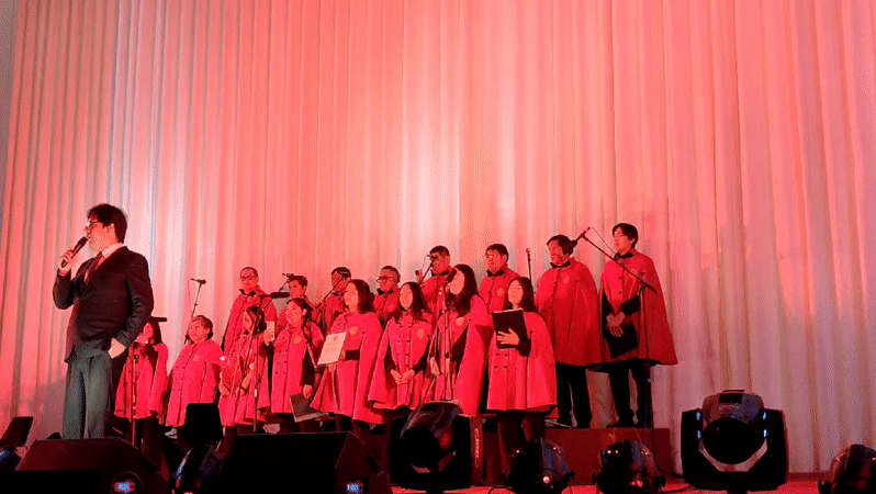 Red-robed choir performs with suited speaker in Cusco