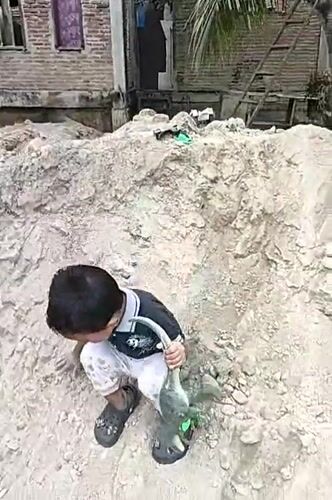 Toy dinosaur in hand, crossing a rocky dirt pile in Indonesia