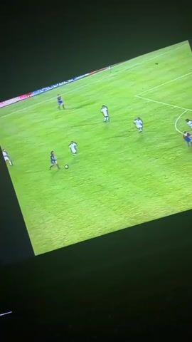 The video shows a television screen displaying a soccer game. A player in a Barcelona jersey kicks the ball toward the goal, and the goalkeeper dives to attempt to block it. The ball goes into the net. The jersey of the player is shown in close up. The score is then displayed: Barcelona 1 X 0 Sevilla. The television is on top of a keyboard. The lighting is low.