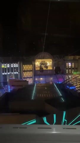 The video shows a nighttime view of a city from inside a cable car. The cable car approaches a station with neon lights and an archway. As the cable car moves away from the station, the view shifts to a large hotel, "First World Hotel, the World's Largest," with many illuminated windows. Below the hotel, a complex of buildings with glass roofs and various colored lights is visible.
