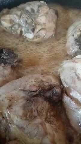 This is a close-up, top-down video of chicken pieces cooking in a pot. The chicken is browned and appears to be simmering in a liquid that is bubbling. The lighting is dim and natural.