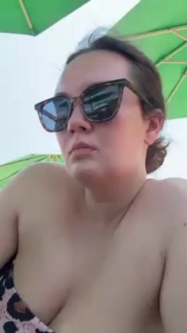 A woman in a leopard-print bikini top and sunglasses is sitting under a green umbrella. She takes a drink from a can of Pepsi Zero, then lowers it and looks to the side, seemingly satisfied. Her hair is pulled back.