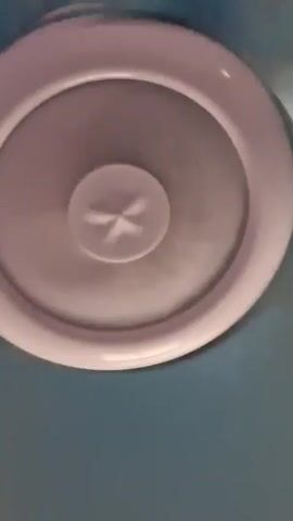 The video shows a close-up, upward-facing view of a white ceiling fan with a light in the center. The fan blades are spinning, creating a blurred effect. The surrounding ceiling is a light blue color. The lighting is dim and the focus is on the spinning fan.
