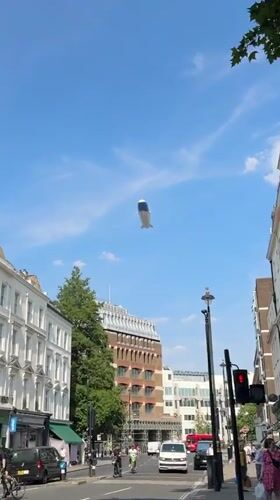 Blimp drifts over a busy London street on a summer afternoon