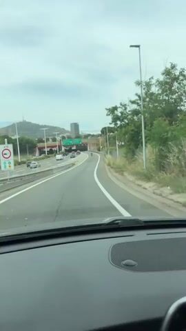 The video captures a car driving on a multi-lane highway with an exit ramp to the right. The view is from inside the car, looking through the windshield. There are several cars on the road, and a tunnel or underpass is visible in the distance. A McDonald's billboard is on the right side of the road. The sky is cloudy.