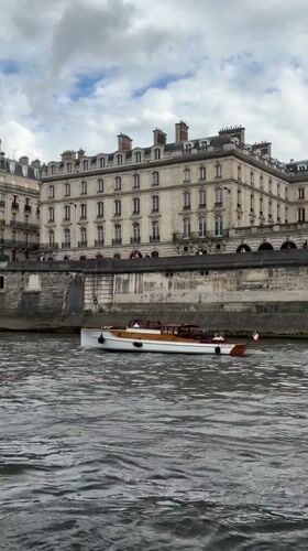 Passenger boat travels Seine River past Parisian stone embankment