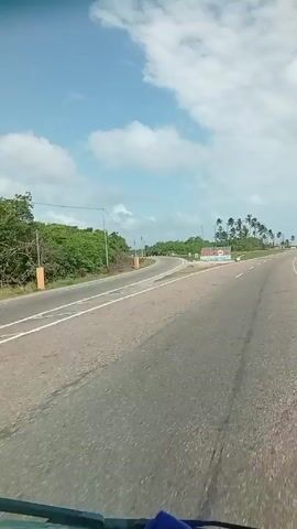 The video shows a drive into Falcón, Venezuela. The camera pans across a sign that reads “Falcón” with the tagline “Lo Tiene Todo”. Palm trees are visible, as well as the ocean in the distance.  The camera shakes due to the motion of the vehicle.