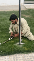 Man trims grass with shears in Quetta City